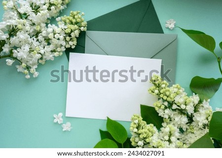 Composition with empty green envelope and beautiful spring lilac flowers on mint background. Mockup card invitation greeting card postcard copy space template. Branches of lilac blooming bouquet.  Royalty-Free Stock Photo #2434027091