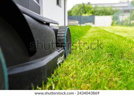 Mowing grass with an electric, powered mower, with a cutting width of 44 cm, visible mown rows. Royalty-Free Stock Photo #2434043869