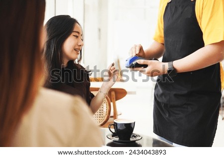 Happy young woman paying bill with a contactless credit card in a coffee shop cafe restaurant. Female smiling holding a creditcard and giving a payment transaction to the cashier. High quality photo. 