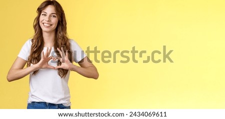 You my valantine. Tender confident adult girl curly hairstyle show heart gesture near chest express romantic sympathy feelings smiling delighted cherish relationship boyfriend yellow background.