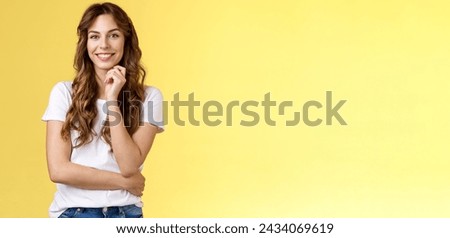 Intrigued attractive european brunette curly long hair look interested listen curious suggestion touch cheek interest temptation smiling toothy pleased good conversation stand yellow background. Royalty-Free Stock Photo #2434069619