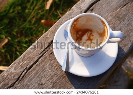 Coffee cup placed on wooden log with sunlight. Cup of coffee top view welcomes new morning. Hot latte coffee in a cup and spoon. The concept of happiness of being alone and enjoying the atmosphere. 