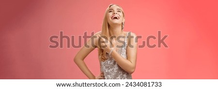 Fabulous carefree attractive blond woman in silver evening party dress laughing out loud have fun raise hand joyfully up pointing right index finger enjoying awesome sense humour, red background.