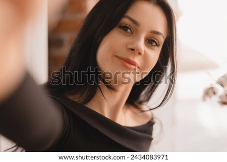Pensive brunette woman make selfie posing on cafe outdoors background. Outdoor shot of happy hippie teen lady make video call. Girl wear black long sleeves top, look at camera.