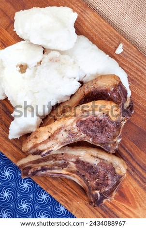 three lamb rib chops with pap or maize meal on rustic chopping board and traditional South African fabric with copy space Royalty-Free Stock Photo #2434088967