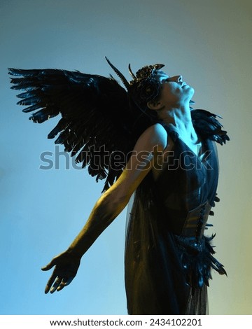 Close up portrait of female model wearing gothic horned headdress, halloween black dress and fantasy angel feather wings. Isolated dark studio background with cinematic shadow silhouettes 