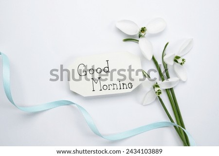 Good morning and snowdrops. Good morning written on a papper blank on a white background with the first flowers of snowdrops, top view, flat lay.