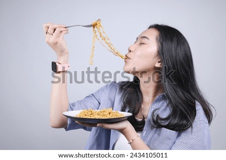 Young Asian girl enjoying eating delicious fried noodles with fork, side view