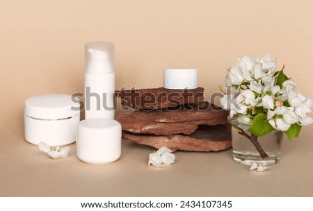 White jars of skin care natural floral cosmetic products on stone podium or pedestal and apple tree flowers. Cosmetics with apple extract. Spring facial skin care. Front view, copy space, mock up