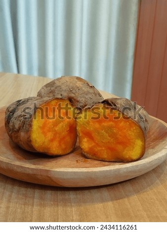 This picture was taken on March 6, 2024. its a few pieces of sweet potato placed on wooden plate on a wooden table with gray curtain for background 
