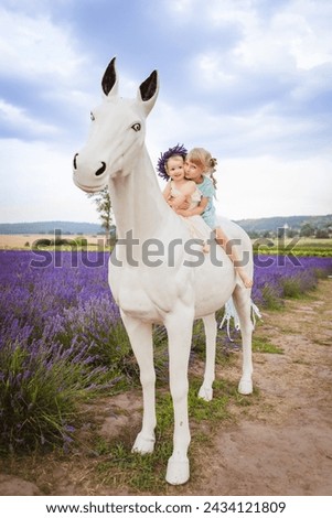 On a lavender field there is a picture of two sisters sitting on a white decorative horse