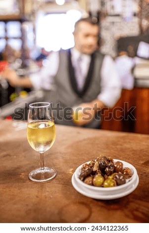 A glass of fino sherry with a side of mixed olives on a bar in a traditional Seville tavern. Royalty-Free Stock Photo #2434122365
