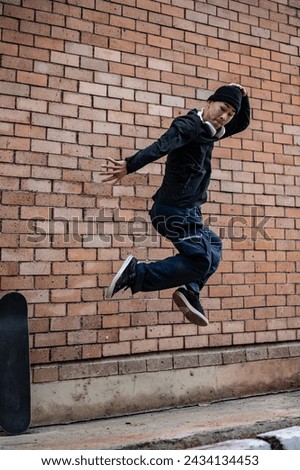 A cool, energetic Asian man in fashionable clothes is jumping outdoors, practicing his breakdance on the street. Royalty-Free Stock Photo #2434134453