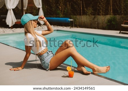 Attractive young woman with a blue cap sitting by the pool 