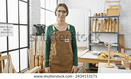 Confident woman carpenter with safety glasses stands in a well-equipped woodworking workshop.
