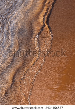 Ocean surf on sandy beach, top view. Nature background with red sand and waved lines of seawater on a sand shoreline. Royalty-Free Stock Photo #2434156537