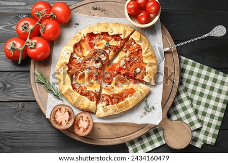 Tasty galette with tomato and cheese (Caprese galette) on black wooden table, top view