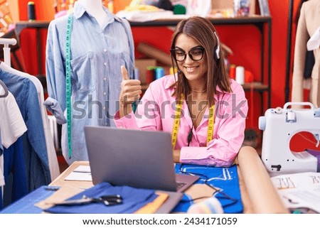 Young hispanic woman dressmaker designer doing video call with laptop smiling happy and positive, thumb up doing excellent and approval sign 
