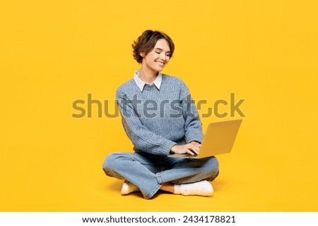 Full body happy smart young IT woman she wears grey knitted sweater shirt casual clothes sits hold use work on laptop pc computer isolated on plain yellow background studio portrait. Lifestyle concept