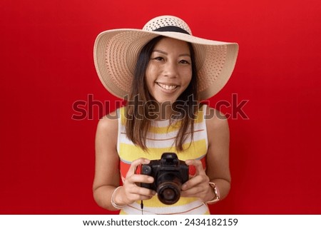 Middle age chinese woman using reflex camera wearing summer hat smiling and laughing hard out loud because funny crazy joke. 