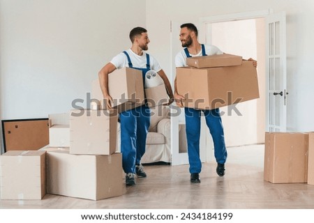Front view, holding stuff. Two moving service employees in a room. Royalty-Free Stock Photo #2434184199