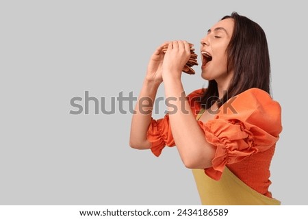 Young woman eating tasty pancakes on grey background