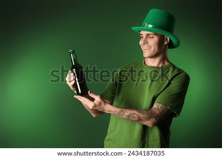 Young man with bottle of beer on dark green background. St. Patrick's Day