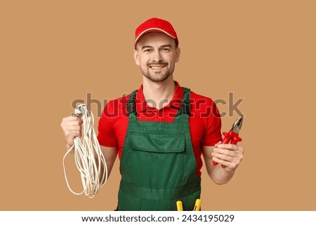 Portrait of male electrician with pliers and wires on beige background Royalty-Free Stock Photo #2434195029