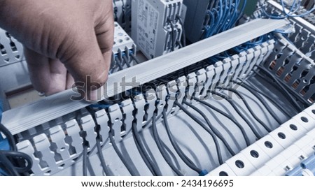 an electrician's hand is opening or closing the circuit cable cover on the electrical control panel board.Check and repair electrical trouble concept. Royalty-Free Stock Photo #2434196695