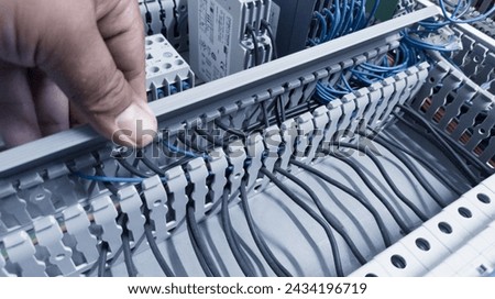 an electrician's hand is opening or closing the circuit cable cover on the electrical control panel board.Check and repair electrical trouble concept. Royalty-Free Stock Photo #2434196719
