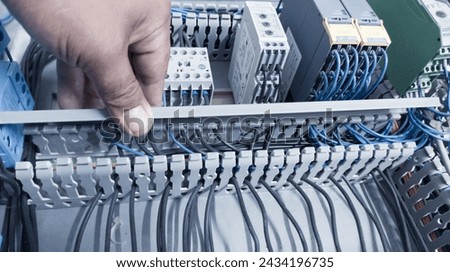 an electrician's hand is opening or closing the circuit cable cover on the electrical control panel board.Check and repair electrical trouble concept. Royalty-Free Stock Photo #2434196735