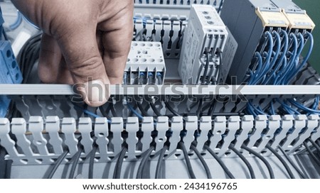 an electrician's hand is opening or closing the circuit cable cover on the electrical control panel board.Check and repair electrical trouble concept. Royalty-Free Stock Photo #2434196765