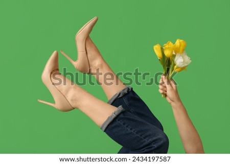 Legs of beautiful young woman in high heels with tulips flowers on green background