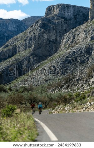Young and Mid Adult Friends Cycling Up Rural Mountain Road, Alicante, Costa Blanca, Spain - stock photo