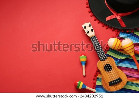 Mexican sombrero hat, maracas, guitar and colorful poncho on red background, flat lay. Space for text