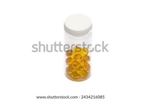 Closed transparent vial with small round yellow capsules, on white background