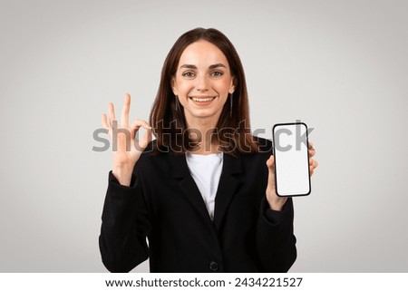 Cheerful caucasian millennial businesswoman showing a blank smartphone screen and making an 'okay' sign, indicating approval or a positive review of a mobile app or service