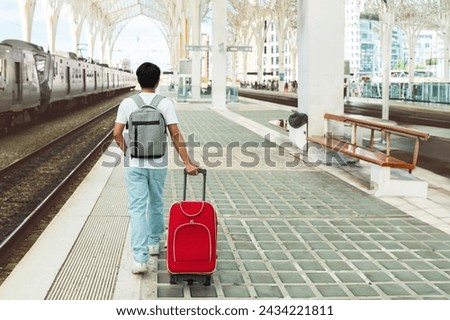 Back view of young man tourist walking by train station, carrying suitcase and backpack, waiting for his train. Guy student traveling solo, full length, copy space Royalty-Free Stock Photo #2434221811