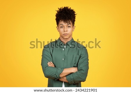 Confident handsome african american man wearing green shirt posing isolated on orange studio background, holding arms crossed on chest, looking at camera, copy space