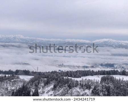 Drone photo: Snowy mountains covered with deep white snow and a rural town surrounded by a sea of ​​clouds