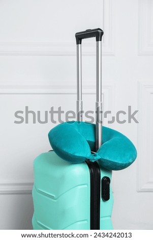 Turquoise travel pillow on suitcase near white wall