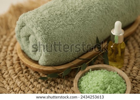 Spa composition. Rolled towel, cosmetic product, sea salt and twig on wicker mat, closeup
