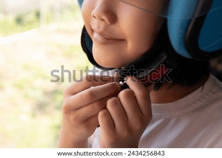 Closeup image of Asian kid smiling and buckling motorcycle helmet. Copy space for text. Royalty-Free Stock Photo #2434256843