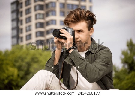 The guy looks into the lens.Young man taking pictures.photography courses.Man holding camera in his hands.Photoshoot.Photographer in nature.Street photography.learning camera settings