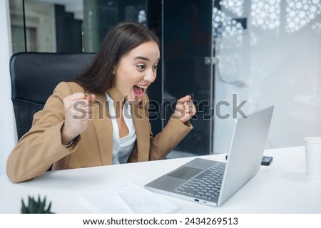Excited cheerful young woman using laptop computer at office getting good news, feeling joy Royalty-Free Stock Photo #2434269513