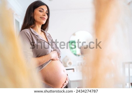 Comfortable beauty pregnant woman standing touching her belly at home