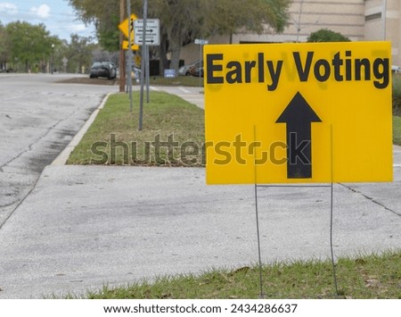 Early Voting sign with black directional arrow on grassy area by sidewalk
