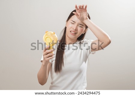Suffering summer heat wave stroke, hot weather, tired asian young woman sweaty and thirsty, refreshing with hand in blowing, wave fan to ventilation when temperature high, isolated on background. Royalty-Free Stock Photo #2434294475