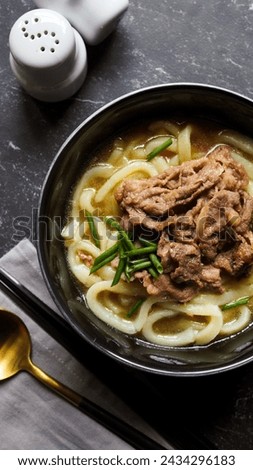 Gluten free chewy udon. Thick noodle made with rice flour and tapioca starch, served with tasty broth and stir fried sliced beef. Over black marbled background. Top view