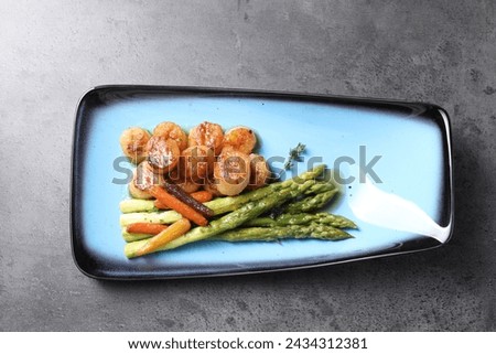 Delicious fried scallops with asparagus and vegetables on grey table, top view